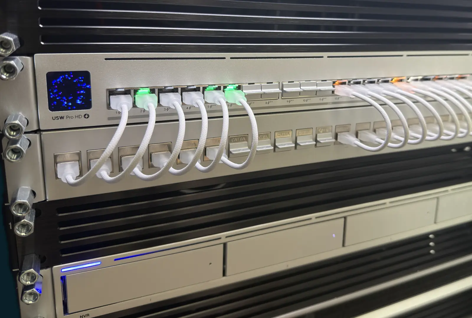 UniFi rack with a UDM Pro Max gateway, a USW Pro HD switch patched with short white cables, and a network video recorder